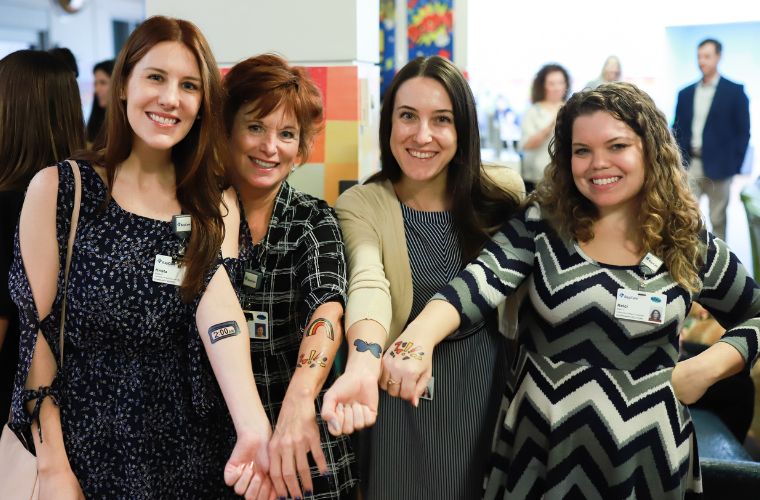 Four women with their arms outstretched show their temporary tattoos.