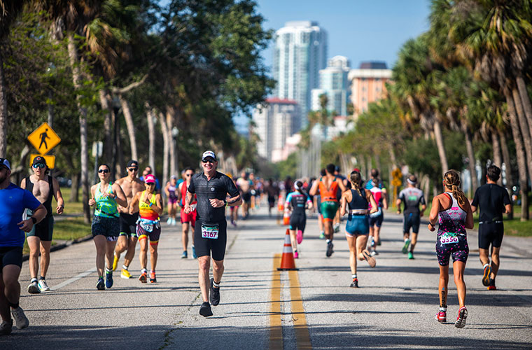 Men and women dressed in athletic clothes with numbers pinned to them run down a street in a race.