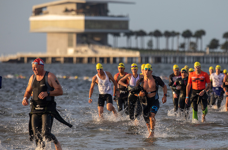 Men dressed in swim gear, wetsuits and yellow swim caps prepare for a swimming competition.