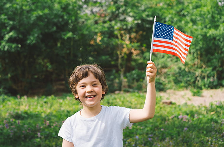 A young boy holding a small American flag and smiling