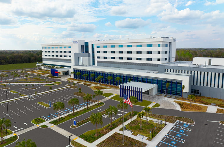 An aerial view of the new South Florida Baptist Hospital in an empty parking lot. The building is large and rectangular.