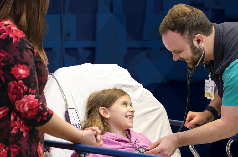 Report to the Community booklet cover featuring photo of smiling young female patient holding her mother’s hand as a BayCare pediatric resident examines her in the pediatric emergency department at St. Joseph’s Children’s Hospital.