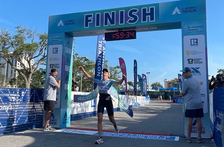 A woman dressed in athletic clothing stretches her arms and looks upward as she prepares to cross the finish line in a competition.