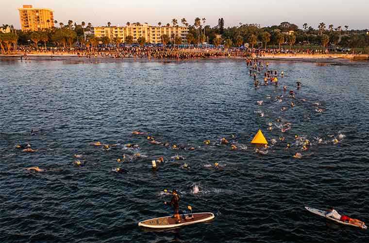 Men dressed in swimsuits and swim caps make their way into the water for the beginning of an athletic competition.