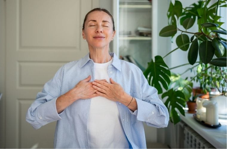 A woman is holding her chest, appearing to take deep breaths, conveying a sense of calm and introspection.