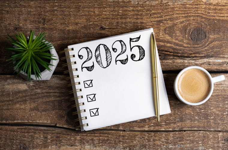 A visual representation of 2025 goals and resolutions, with a notebook in the center of the screen, a coffee cup to the right and a plant on left.