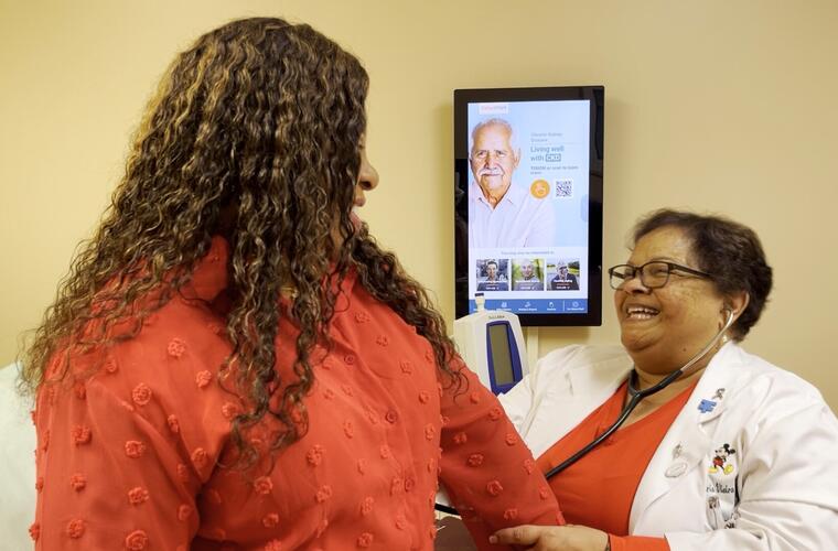 A woman in a red shirt engages in conversation with a nurse practitioner in a clinical setting.