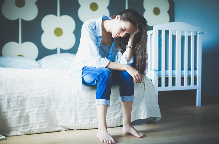 Tired mother sitting on bed near a baby crib.