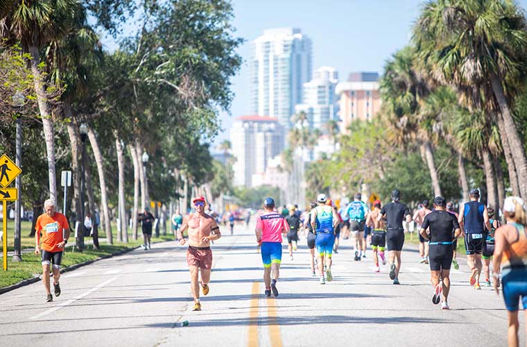 People in an athletic competition run past homes and palm trees.