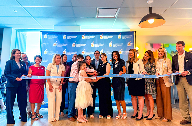A group of people standing behind a blue ribbon being cut by a young girl.