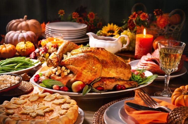 A festive Thanksgiving table featuring a golden roasted turkey surrounded by seasonal sides, a pie, candles and autumn decorations.