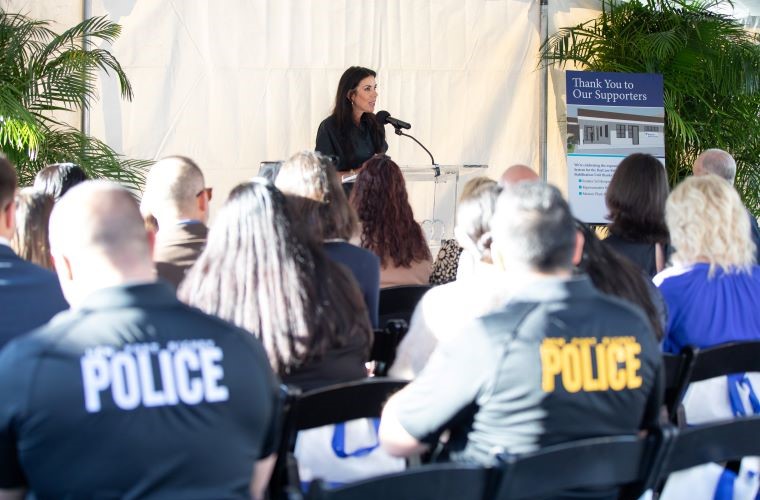 A woman speaking into a microphone addresses a crowd at an outdoor event.