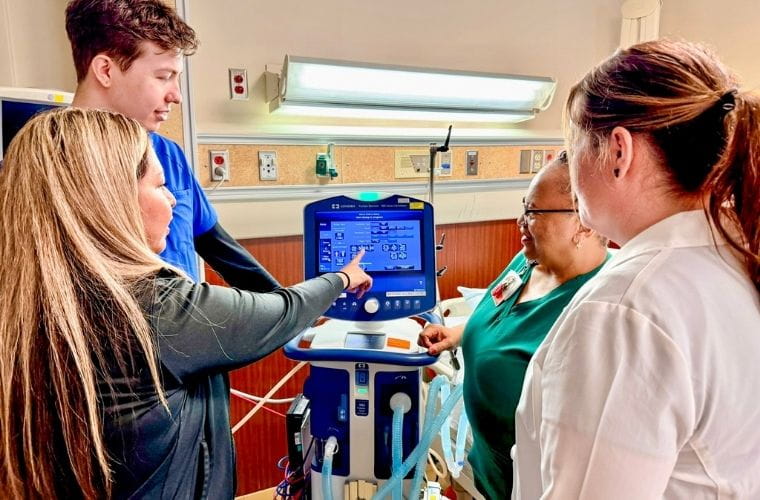 Clinical team members reviewing settings on a hospital respiratory care machine.