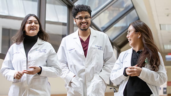 A group of three BayCare resident physicians talk while they walk through the halls of the hospital.