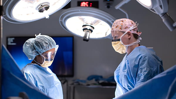 Two physicians stand over an operating table with lights overhead.