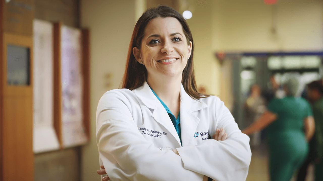 A female hospitalist at BayCare smiling with her arms crossed in a hospital setting.