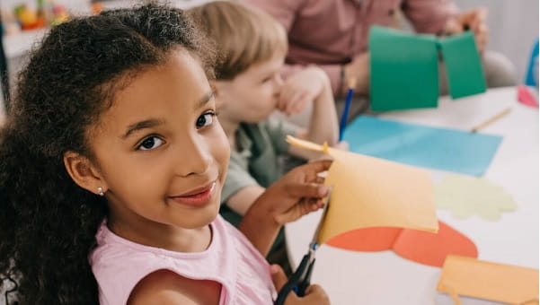 little girl cutting construction paper with a group of kids at school