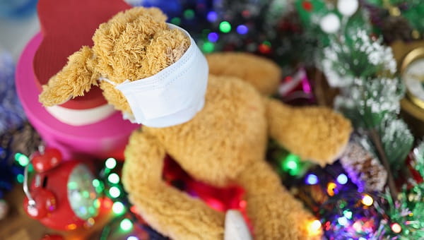A stuffed animal is wearing a mask and sitting on top of Christmas decorations.