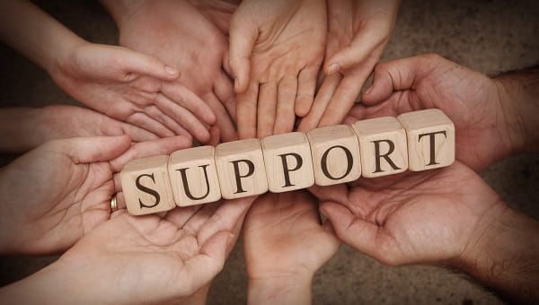 Hands are holding up wood blocks that spell the word "support."