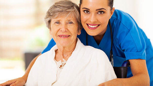 A smiling female nurse visiting with a senior female patient
