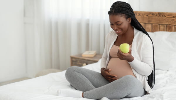 Young female sitting on a bed eating an apple