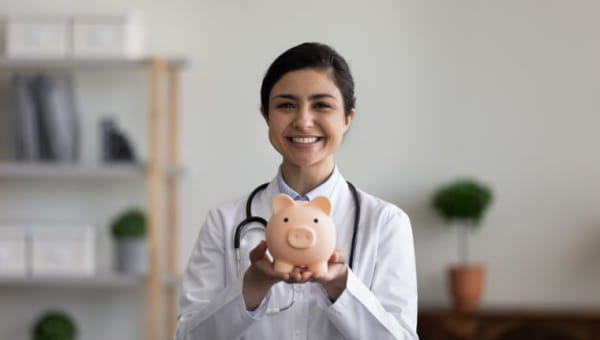 Understanding the Connection Between Financial Wellness and Mental Health A young female health professional smiling while holding a piggy bank.