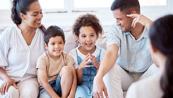 A smiling family sitting on a couch talking with a therapist.
