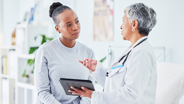 A woman engages with a doctor, holding a tablet, focusing on gynecological cancer care and available treatment programs.