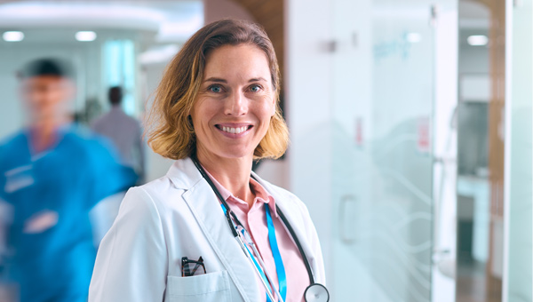 A female healthcare provider in a white lab coat is positioned in a hallway of a women's hospital.