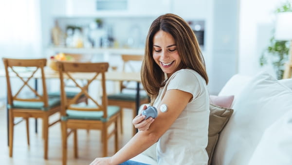 Women applying glucose monitor to arm.