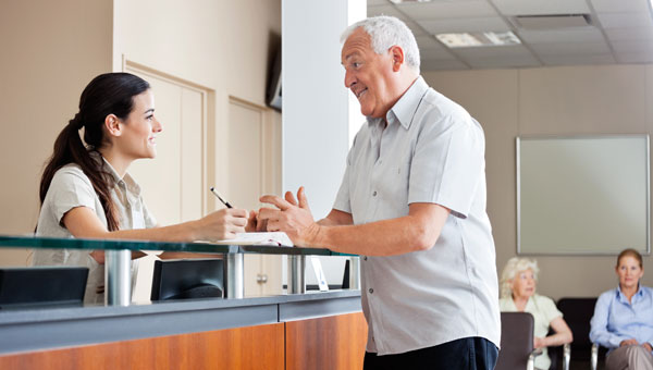 older man speaking with front desk professional inside waiting room
