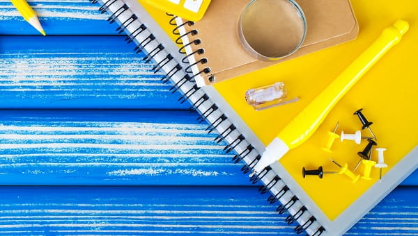 Back-to-school supplies on a table, including notebooks, pencils, a pen, magnifying glass and push pins.