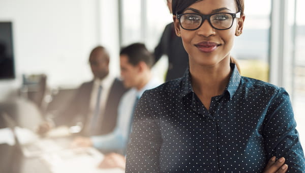 A beautiful young black woman, who is wearing glasses, is smiling in a conference room.