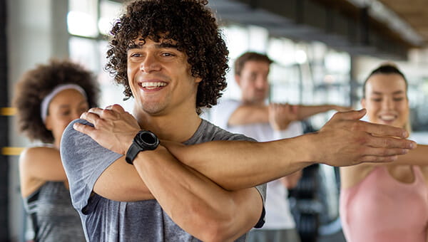 BayCare Fitness Programs A male in a group fitness setting stretching his arms and smiling.