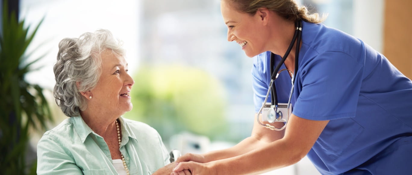 a young female clinician and a senior woman smiling and holding hands