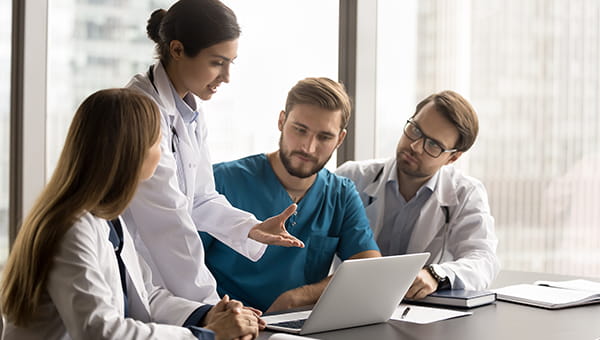 A team of doctors coordinating efforts sitting at a table in front of a laptop