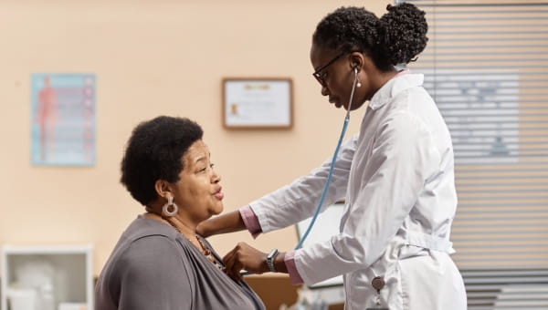 A doctor examining a woman, assessing her for potential heart disease symptoms.