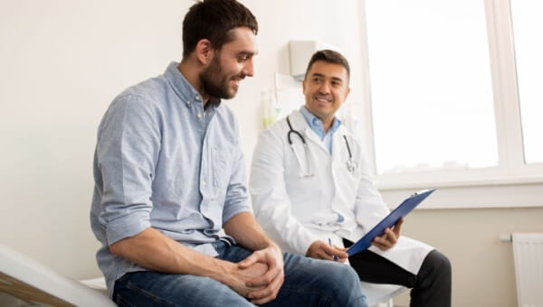 A male doctor sits with a male patient, looking at his patient chart.