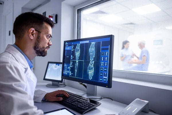 A technician looks at an imaging scan with a patient and nurse in the background.