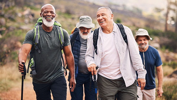 four senior men laughing and smiling while hiking on a dirt trail