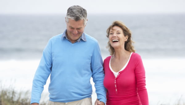 Download Your Total Hip and Knee Surgery Guide Man and woman walking together happily on the beach.