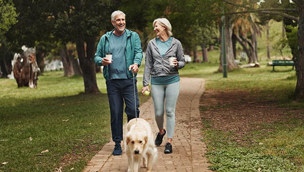 Older couple walking their dog in a park.