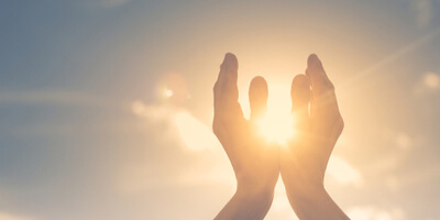 two hands praying and held up to the sky and sun
