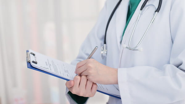 a physician holding and writing on a clipboard