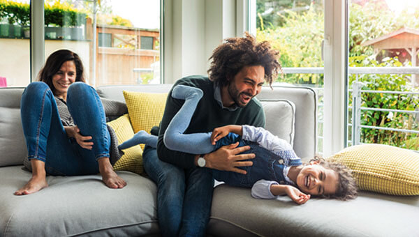 A family of three sitting together on the couch while playing with their child.