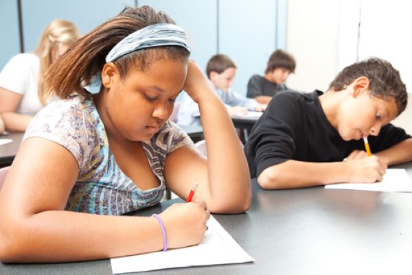 A group of children lean over their desks while working on a test.