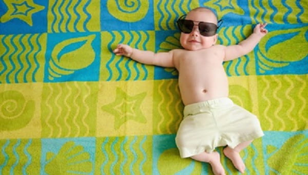 Adorable baby in beach shorts relaxing on a big beach towel smiling