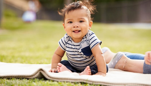 Little baby boy sitting up on a blanket in the park looking to camera close up