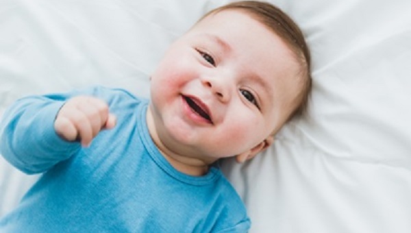 Portrait of an adorable 3 month old baby smiling lying in a bed of white sheets