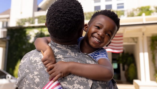 A little boy hugging their parent wearing a military uniform.